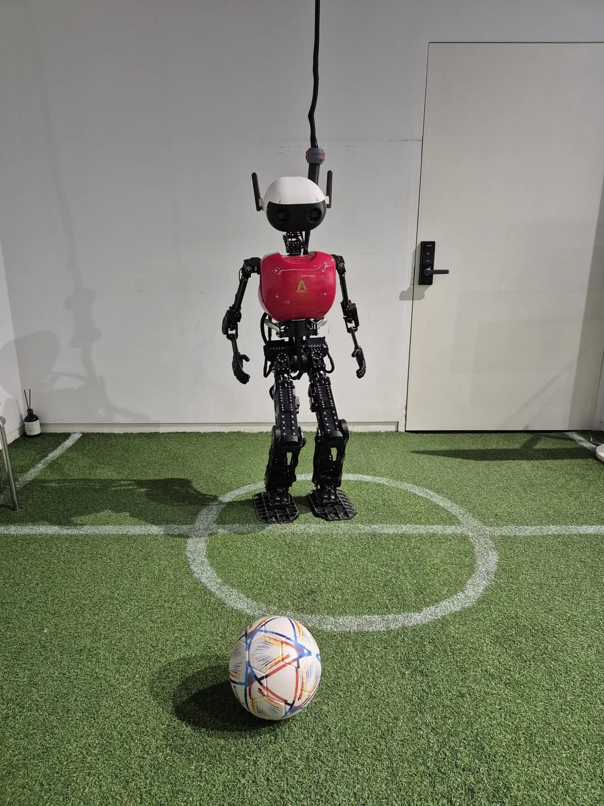 Un pequeño robot humanoide con un balón sobre césped artificial
